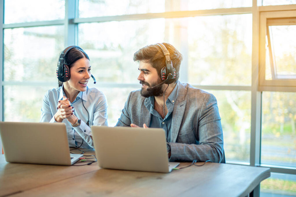 Kaksi liike kollegat kuulokkeet ja kannettava tietokone chattailuun toimistossa - Valokuva, kuva