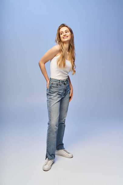 A beautiful blonde woman strikes a pose in a tank top and jeans in a studio setting. - Photo, Image