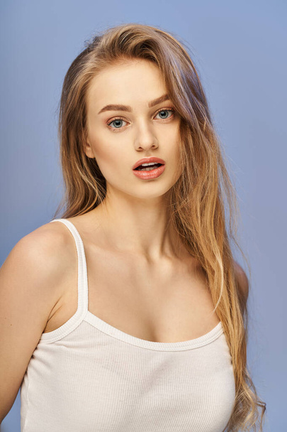 A young blonde woman in a white top striking a pose in a studio setting, exuding elegance and grace. - Photo, Image