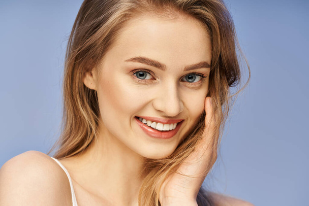 Une jeune, belle femme aux cheveux blonds frappant une pose, souriant joyeusement pour une séance photo professionnelle dans un cadre studio. - Photo, image
