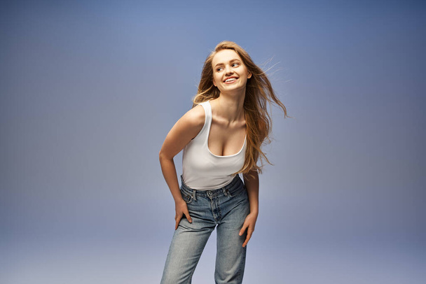 Een jonge blonde vrouw in een tank top slaat een pose in een studio setting, stralende schoonheid en vertrouwen. - Foto, afbeelding