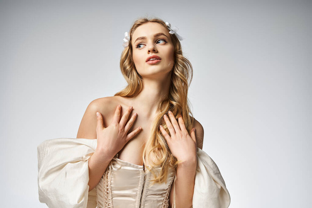 Eine junge, blonde Frau posiert elegant in einem weißen Kleid in einem Studio für ein atemberaubendes Porträt. - Foto, Bild