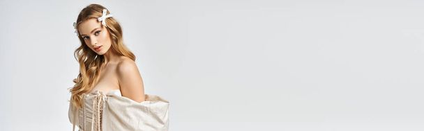 Una joven rubia exuda gracia y elegancia mientras posa para un retrato en un vestido blanco en un ambiente de estudio. - Foto, Imagen