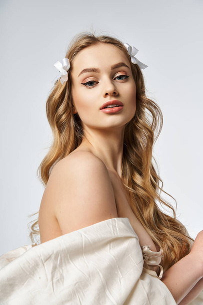Eine junge, blonde Frau strahlt Anmut in einem fließenden weißen Kleid aus und präsentiert ihre langen Haare in einem Studio-Setting. - Foto, Bild