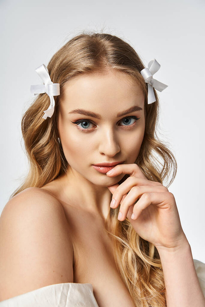 A young, blonde woman with long hair adorned with a white bow in a studio setting. - Photo, Image