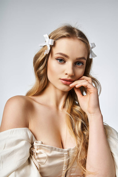 A young, blonde woman exudes tranquility with a white bow gracefully adorning her hair in a studio setting. - Photo, Image