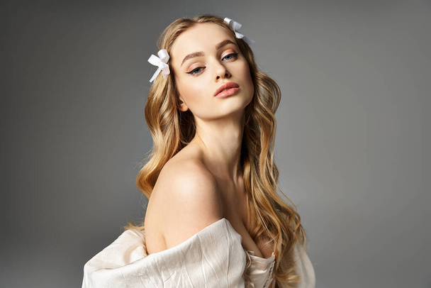Une jeune femme blonde se tient élégamment dans une robe blanche, une seule fleur nichée dans ses cheveux, exsudant un air de grâce et de beauté. - Photo, image