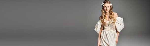 Eine junge blonde Frau strahlt Anmut und Eleganz aus, als sie in einem weißen Kleid in einem Studio-Setting steht. - Foto, Bild