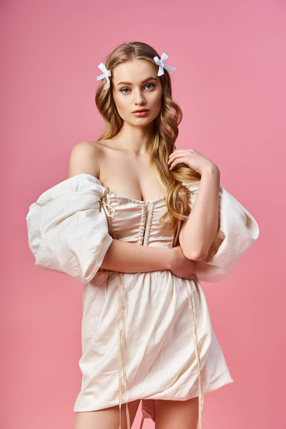 Une jeune femme blonde exsudant élégance et grâce tout en posant dans une robe blanche dans un décor de studio. - Photo, image