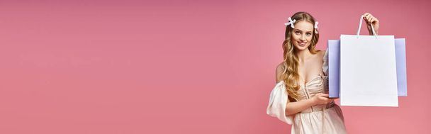 Una mujer joven y rubia con un vestido elegante sostiene con gracia una bolsa de compras en un entorno de estudio. Ella exuda elegancia y aplomo. - Foto, imagen