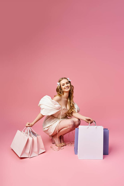 Eine junge schöne blonde Frau kniet elegant auf dem Boden, umgeben von Einkaufstüten. - Foto, Bild