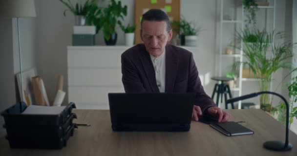 Hombre de negocios serio hablando en el teléfono móvil mientras trabaja en el ordenador portátil en el escritorio en la oficina - Metraje, vídeo