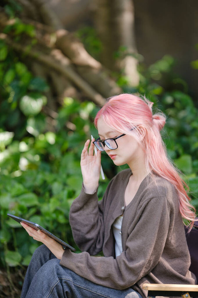 Linda chica de pelo rosa dibujando en tableta digital en el jardín, Mujer haciendo trabajo independiente en el jardín, mujer con tableta digital con obras de arte de graffiti. Foto de alta calidad - Foto, Imagen