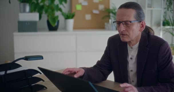 Шокований старший бізнесмен закриває ноутбук за столом під час роботи в корпоративному офісі - Кадри, відео