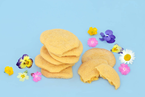 Σπιτικά μπισκότα λευκής σοκολάτας με διάσπαρτα ανοιξιάτικα λουλούδια και αγριολούλουδα σε μπλε φόντο. Φυσική άνεση τροφίμων floral φύση σύνθεση. - Φωτογραφία, εικόνα