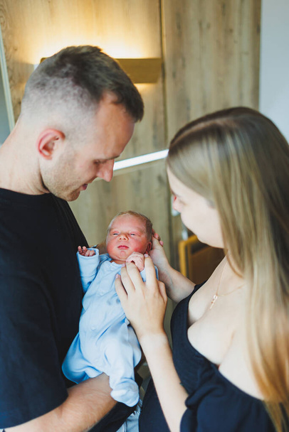 Boldog fiatal szülők, akik az újszülöttjüket tartják a karjaikban. Romper egy újszülött fiún. Az újszülött anya és apa kezében van. - Fotó, kép