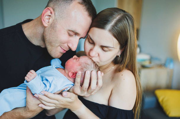 Happy young parents holding their newborn baby in their arms. Romper on a newborn boy. Newborn baby in the hands of mom and dad - Foto, Imagen