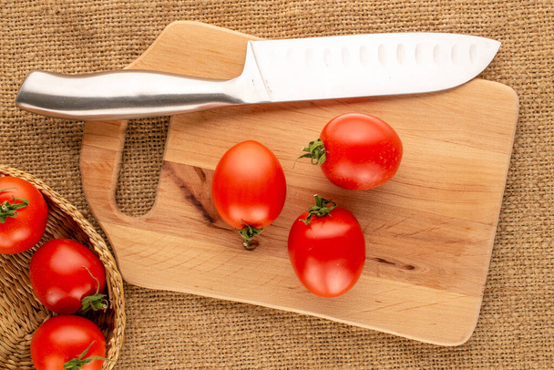 Kilka pomidorów koktajlowych z nożem i drewnianą deską kuchenną na ściereczce z juty, makro, widok z góry. - Zdjęcie, obraz