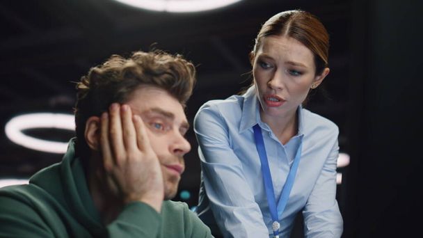 Upset team talking computer office closeup. Worried woman supporting overworked man at evening data center. Tired software developer looking pc screen solving hard task at late night server room  - 写真・画像