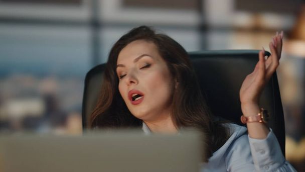 Нервный менеджер, ругающийся с ноутбуком, звонит онлайн на вечернем закрытии офиса. Эмоциональная деловая женщина, агрессивно разговаривающая с компьютером в комнате с панорамными окнами. Нервная женщина ругает подчиненных - Фото, изображение