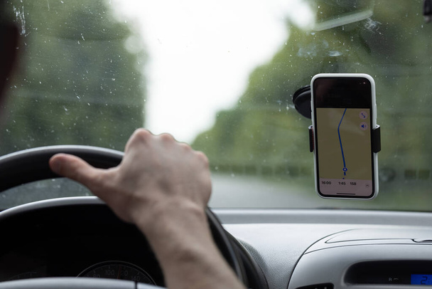 Homem dirigindo um carro com as mãos no volante, usando uma navegação por satélite, GPS. Pára-brisas sujo de insetos - Foto, Imagem