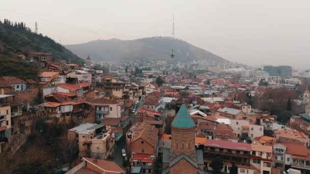 Volo sui tetti della vecchia Tbilisi in tempo nuvoloso in Georgia, il centro storico della città. Veduta aerea dell'antica chiesa cristiana e tetti piastrellati. - Filmati, video