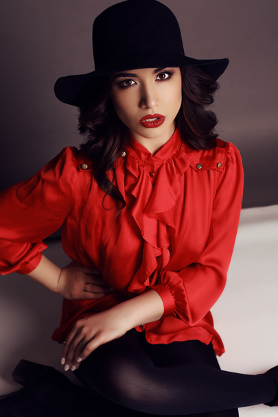 beautiful girl with dark hair in elegant red blouse and black hat   - Foto, Bild