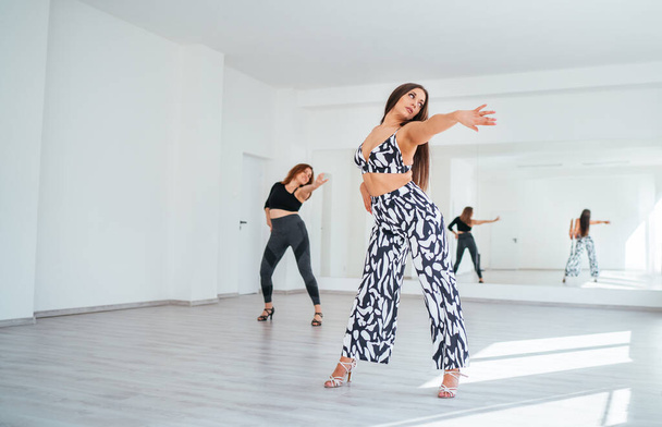 Graceful dancing women group doing elegant dance movements in white color spacious hall with big mirror wall.People's expressions during dancing, beauty of woman's body, active lifestyle concept image - Photo, Image