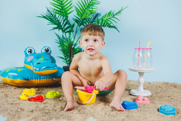 Un bambino in pantaloncini si siede sulla sabbia e gioca con i giocattoli. Vacanze estive. - Foto, immagini