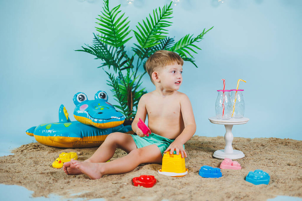 Nyári fotózóna gyerekeknek. Egy rövidnadrágos kisfiú ül a homokon és játszik a játékokkal. Nyári szünet. - Fotó, kép