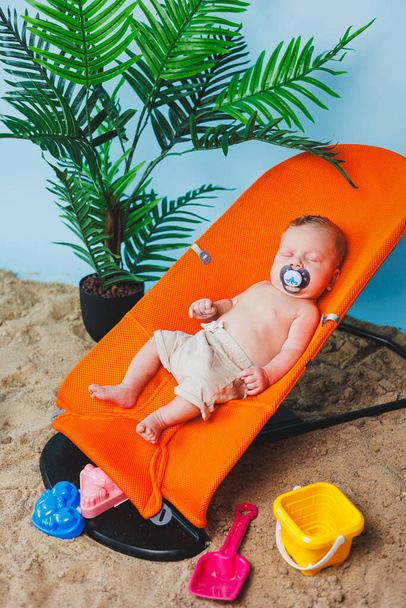 Ένα μικρό νεογέννητο αγόρι κάθεται σε μια καρέκλα μωρού. Παιδική καρέκλα chaise longue. - Φωτογραφία, εικόνα