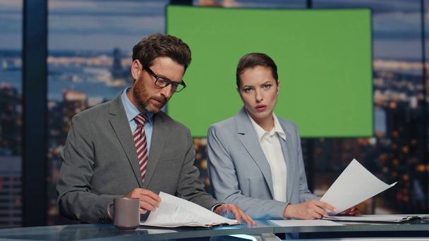 Presenters greenscreen tv studio lighting daily news at evening channel closeup. Elegant confident anchors showing information on chroma key screen. Middle-aged hosts broadcasting newscast in air - Photo, Image
