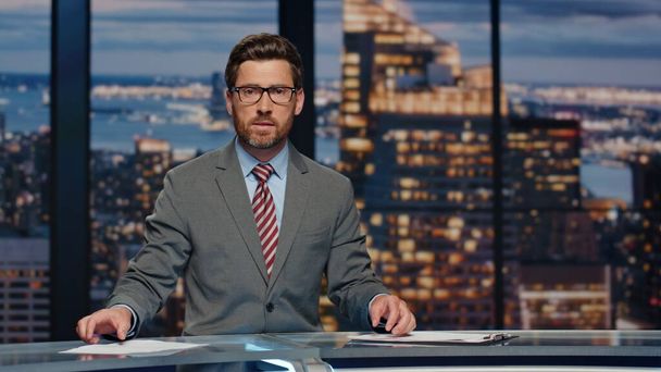 Serious newsreader speaking newscast evening television studio closeup. Confident man host lighting world political situation sitting newsroom desk at light. Professional tv broadcasting concept - Photo, Image