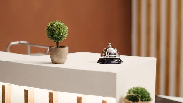 Elegant concierge bell on modern stylish hotel lobby check in desk. Reception bell next to mini plant on empty warm hospitality industry lounge reception counter, close up - Photo, Image