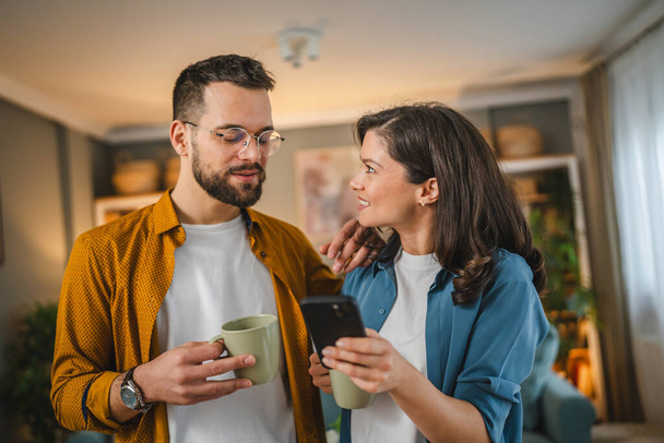 Ενήλικες ζευγάρι άντρας και γυναίκα σύζυγος γυναίκα έχουν ένα φλιτζάνι καφέ χρήση κινητού τηλεφώνου αναζήτηση στο διαδίκτυο κοινωνικό δίκτυο ευτυχισμένο χαμόγελο - Φωτογραφία, εικόνα