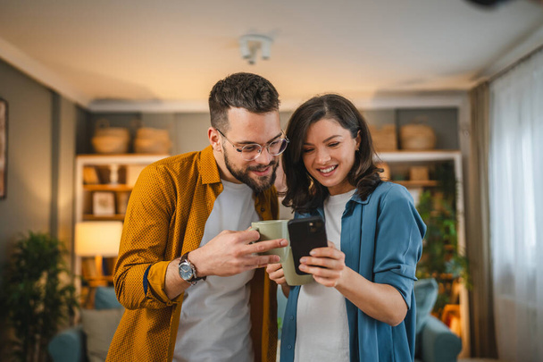 Pareja adulta hombre y mujer marido esposa tienen una taza de café uso teléfono móvil búsqueda internet red social sonrisa feliz - Foto, imagen