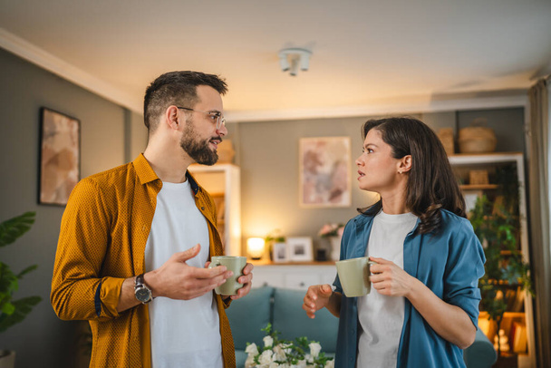 Ζευγάρι άντρας και γυναίκα, άντρες και γυναίκες στέκονται στο σπίτι με ένα φλιτζάνι καφέ, μιλάνε για χαρούμενο χαμόγελο. - Φωτογραφία, εικόνα