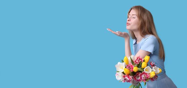 美しいチューリップの花束が付いているかなり若い女性はテキストのためのスペースが付いているライトブルーの背景に対してキスを吹きます - 写真・画像