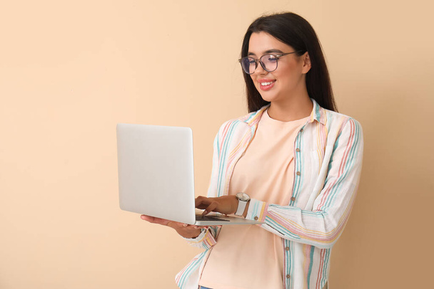 Young happy female programmer working with laptop on beige background - Photo, Image
