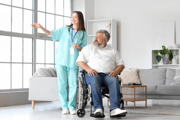 Homem maduro em cadeira de rodas com enfermeira em casa - Foto, Imagem