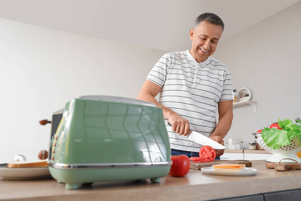 Middle-aged man preparing ingredients for tasty sandwich in kitchen - Photo, Image
