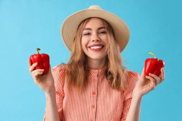 Young female farmer with fresh bell peppers on blue background - Photo, Image