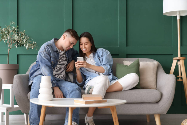 Молода пара використовує мобільний телефон на сірому дивані у вітальні - Фото, зображення