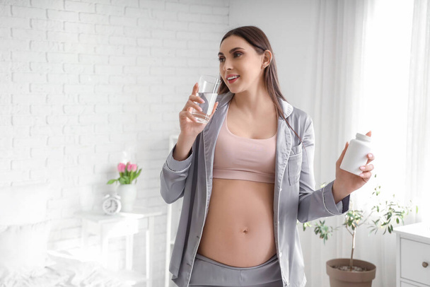 Młoda kobieta w ciąży z butelką z tabletkami i szklanką wody w sypialni - Zdjęcie, obraz