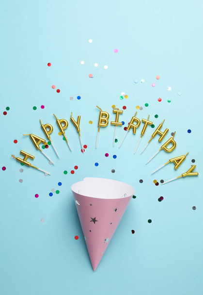 Lettere di candele dorate a forma di felice parola di compleanno con cappello a cono su sfondo blu - Foto, immagini