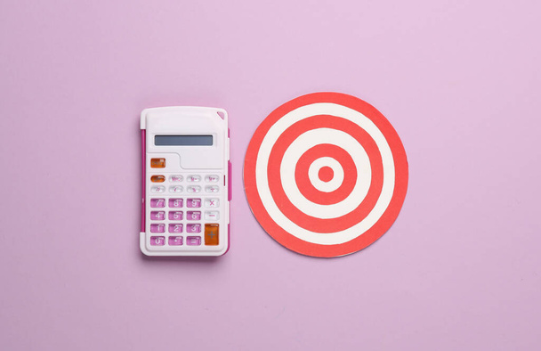 Calculator with a target on a pink background. Business concept - Photo, Image