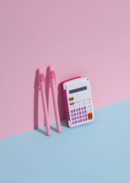 Számológép tollakkal, kék-rózsaszín háttérrel, árnyékkal. Üzlet, oktatás. Kreatív elrendezés, minimalizmus - Fotó, kép