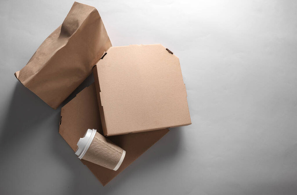Afhaaleten. Geen verspilling. Ambachtelijke kartonnen pizza dozen, koffiebeker, papieren zak op grijze achtergrond. Eco-concept. Bovenaanzicht - Foto, afbeelding