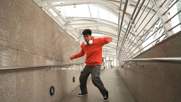 Εξειδικευμένος Ασιάτης χορευτής διαλείμματος δείχνει b-boy step dance στο στενό διάδρομο. Επαγγελματική ενεργητικός hipster κινείται στη μουσική hip hop και φορώντας ακουστικά. Σύγχρονος τρόπος ζωής. Υπαίθριο άθλημα 2024. Ελαφρώς. - Φωτογραφία, εικόνα