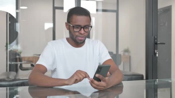 Молодий африканський чоловік святкує успіх на телефоні в офісі - Кадри, відео